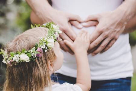 Kind hält Hand auf Babybauch der Mutter