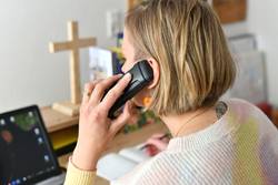 Pfarrerin Nele Schomakers in einem Büro beim Telefonieren - seitlich von hinten aufgenommen mit Blick auf den Bürotisch. In der linken Hand das Telefon, in der rechten Hand ein Kugelschreiber um Notizen zu machen. Im Vordergrund die Hand und der Telefonhörer am Ohr.